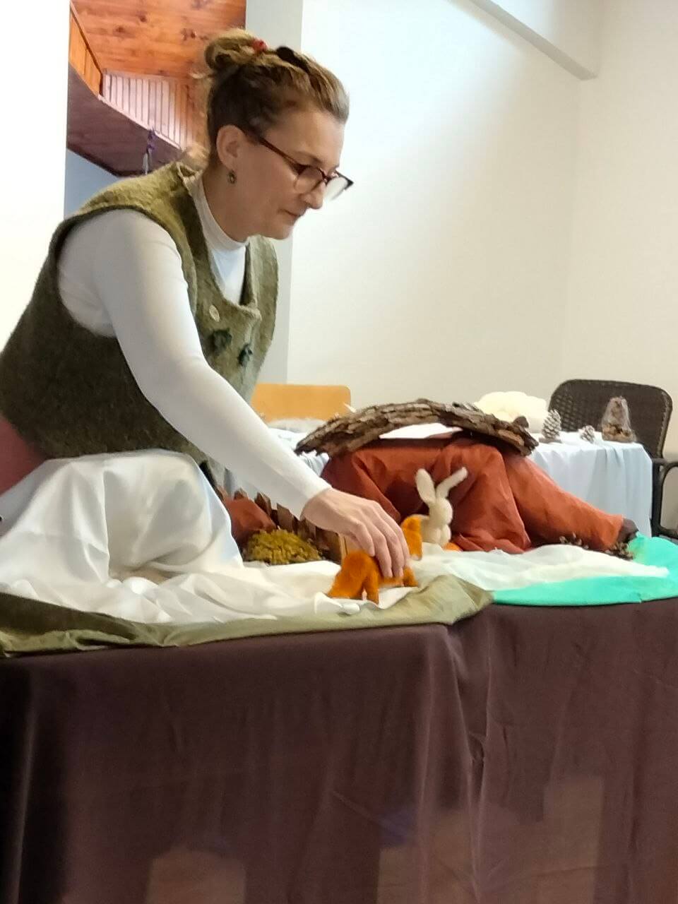 Femeie aranjează scenă cu jucării pe masă.